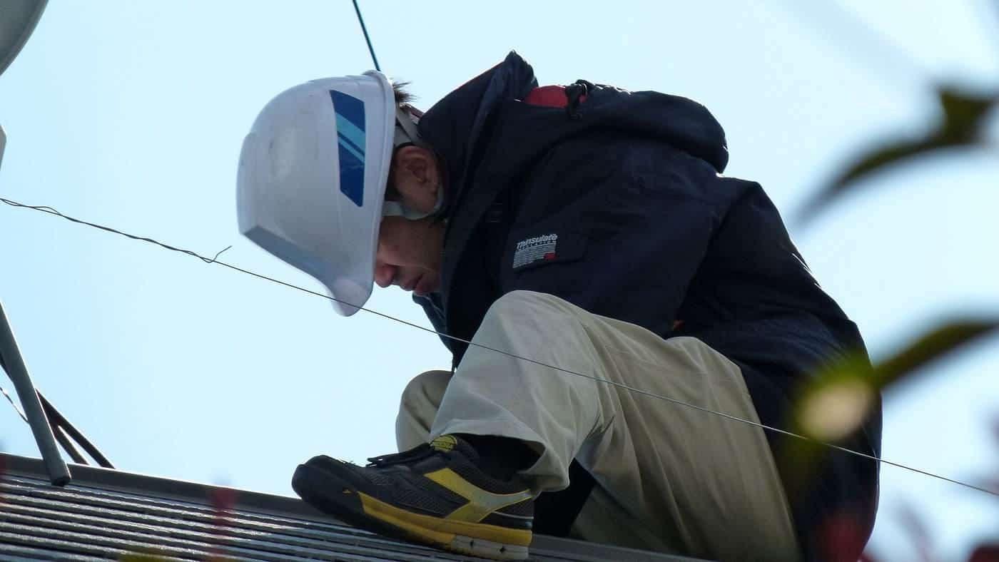 A solar installer in a white hard hat working on a roof
