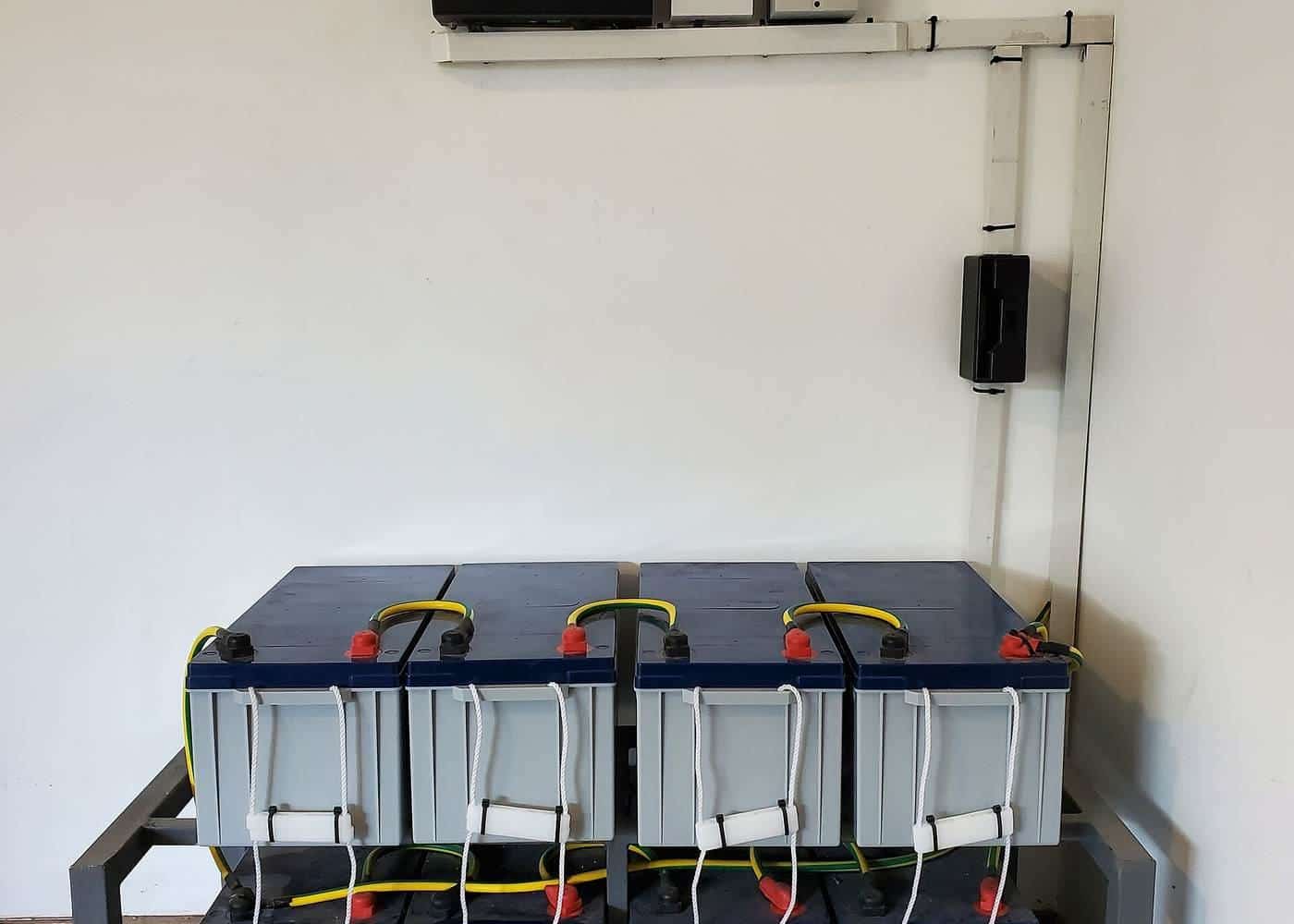 A wall-mounted inverter above a rack of batteries