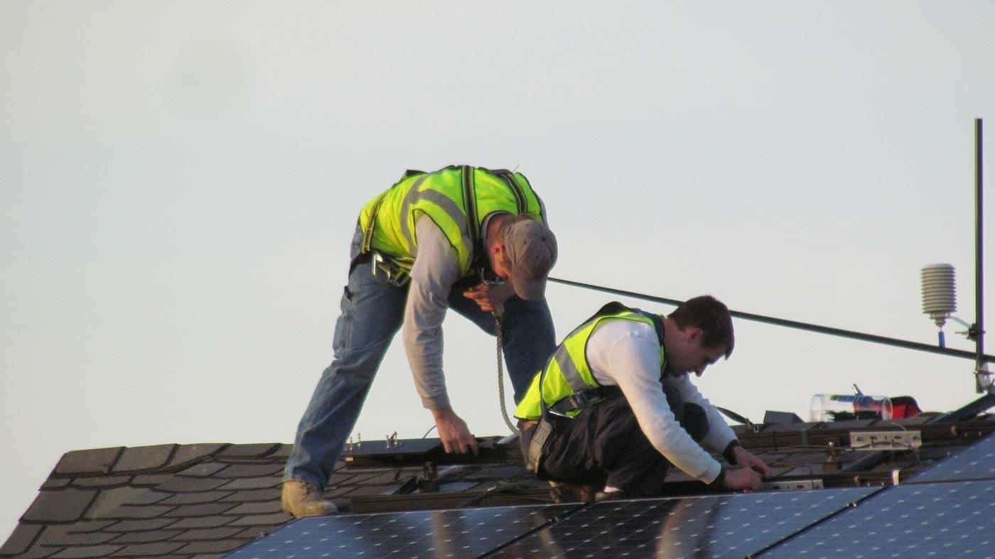 Two installers in high-visibility vests fitting solar panels on a roof