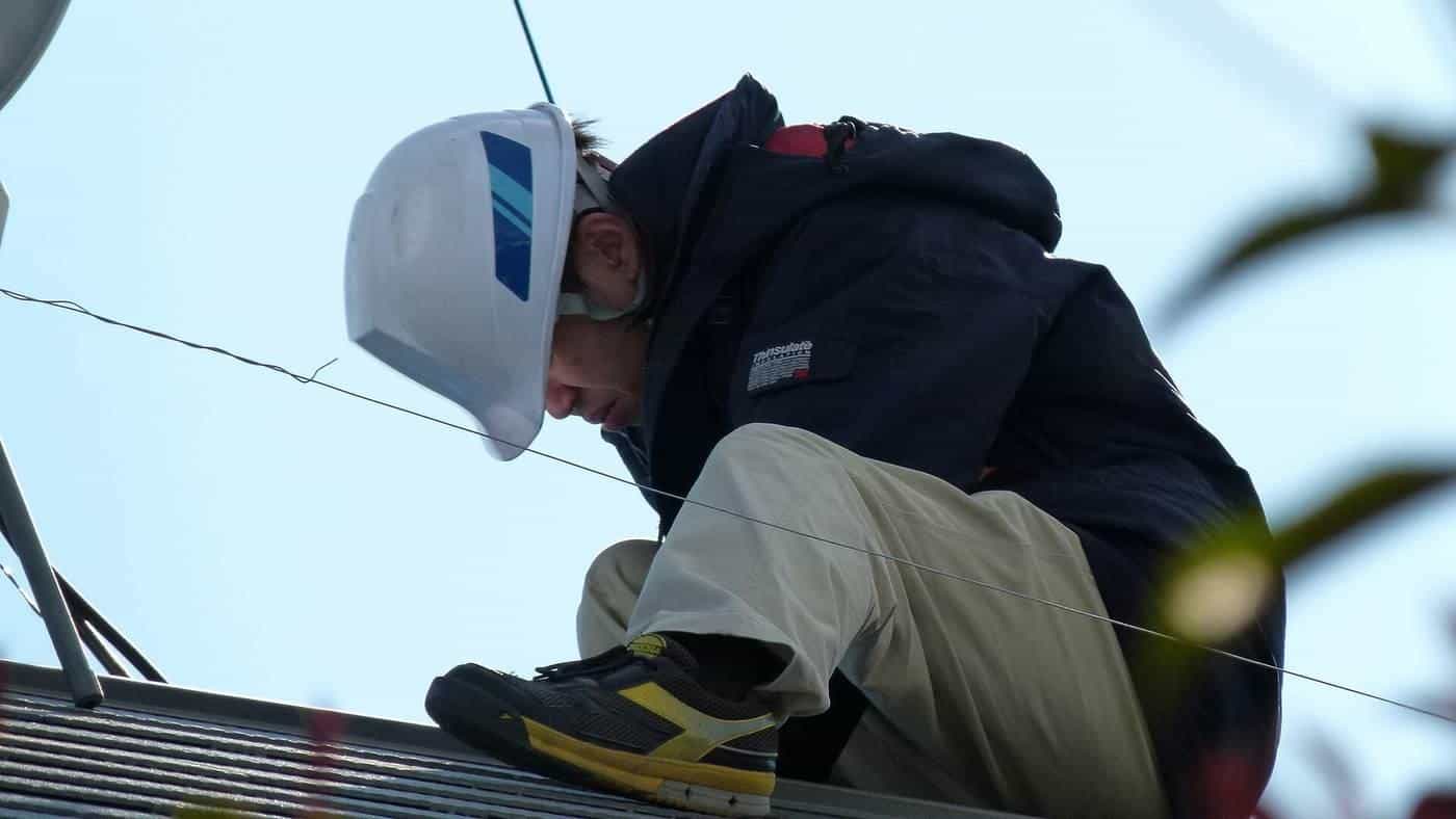 A solar installer in a white hard hat working on a roof