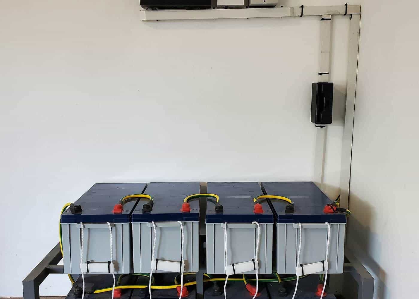 A wall-mounted inverter above a rack of batteries