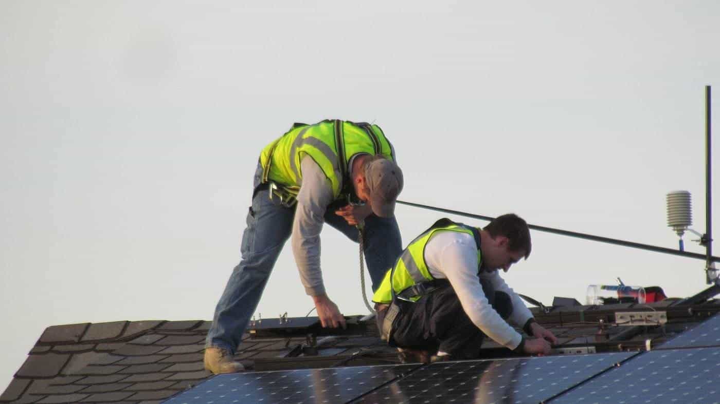 Two installers in high-visibility vests fitting solar panels on a roof
