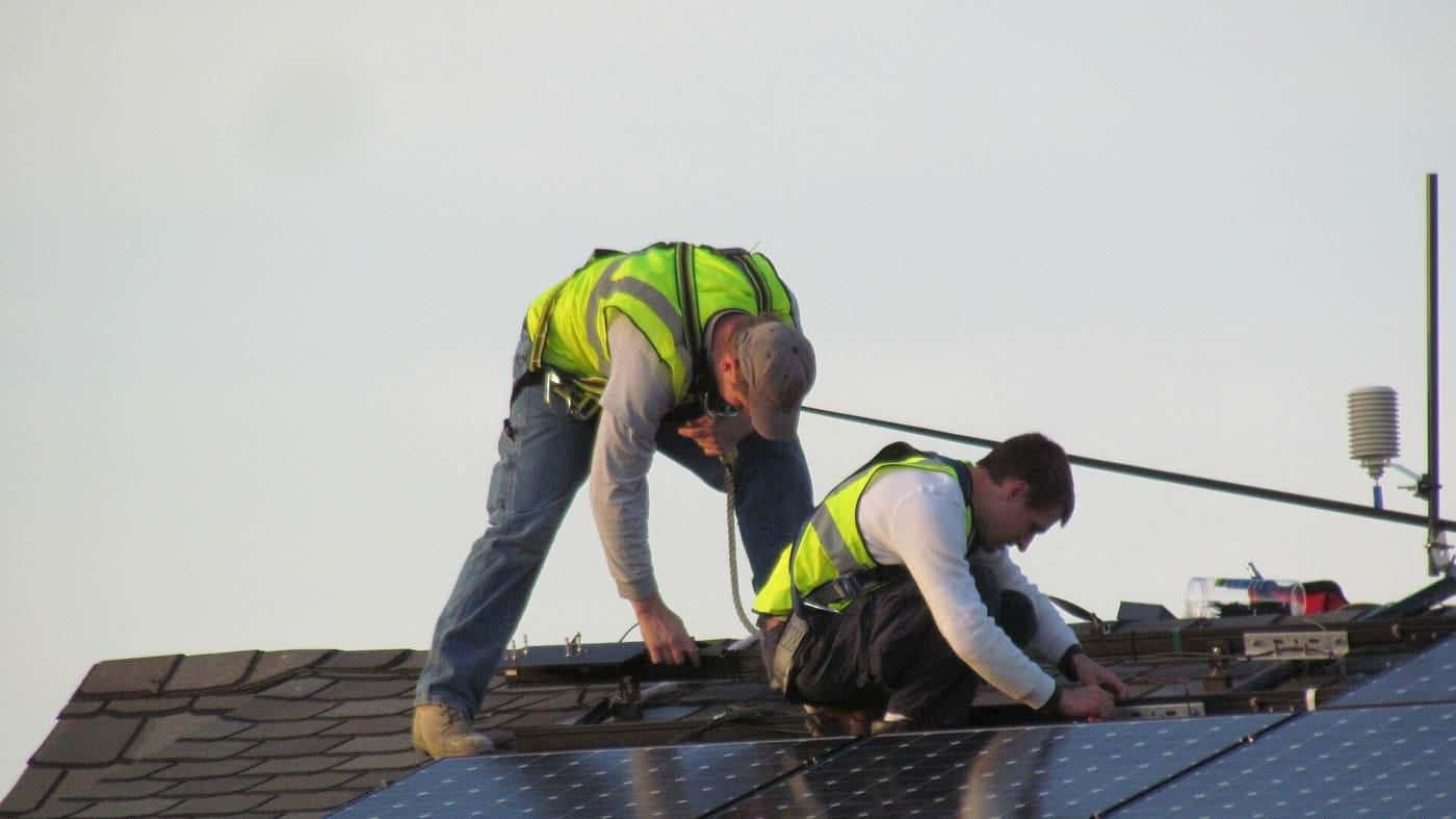 Two workers in high-visibility vests installing solar panels